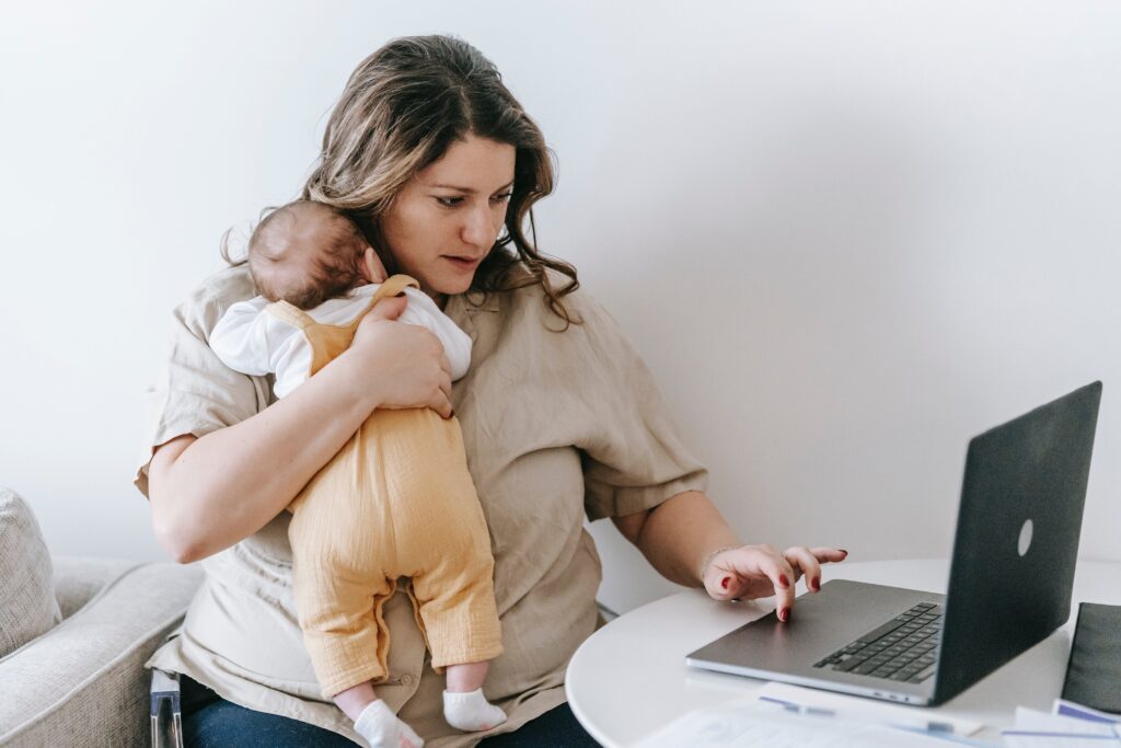 Mom holding baby on her shoulder while working on a laptop.